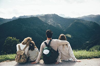 Eine vierköpfige Familie sitzt am Boden eines Weges und blickt in die Berge und durch die wunderschöne Landschaft rund um das Familienhotel Post Family Resort im Salzburger Land.