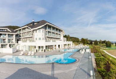 Außenansicht des Familienhotels Aigo welcome family in Oberösterreich. Auf dem Hotelgelände befindet sich ein großer Outdoorpool.