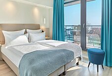 Doppelbett mit Zimmer mit Aussicht nach draußen mit viel Tageslicht im Familienhotel Strandkind an der Ostsee