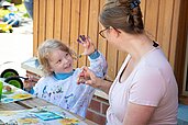 Junge malt gemeinsam mit einer Kinderbetreuuerin im Happy-Club des Familienhotel Landhuus Laurenz.