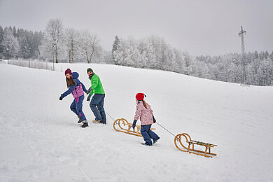 Winter im Thüringer Wald: Familie ist mit dem Schlitten unterwegs. Erlebt ein gemeinsames Rodelabenteuer.