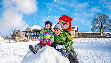 Kinder spielen im Schnee auf dem Hotelgelände mit Clown Happy im Familienhotel Mein Krug.