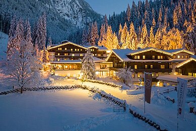 Das Hotel Habachklause im Salzburger Land erstrahlt bei Nacht in festlicher Beleuchtung, eingebettet in eine idyllische, schneebedeckte Landschaft mit dichten Tannen und einem beeindruckenden Berg im Hintergrund.