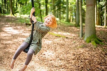 Das Mädchen hat große freude während sie mit dem Tauseil im Waldspielplatz des Familienhotels Landhaus zur Ohe im Bayerischen Wald spielt.