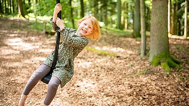 Das Mädchen hat große freude während sie mit dem Tauseil im Waldspielplatz des Familienhotels Landhaus zur Ohe im Bayerischen Wald spielt.