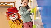 Kinder klettern an der Kletterwand im Happy-Club des Familienhotels Alpenhotel Kindl in Tirol. Auch Clown Happy, das Maskottchen des Familienhotels, klettert mit und bringt die Kinder zum Lachen.