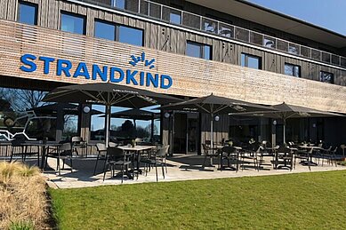 Terrasse mit Sonnenschirmen und Sitzmöglichkeiten zum essen im Familienhotel Strandkind an der Ostsee