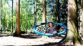 Ein Kind lacht uns sitzt in einer Nestschaukel im Waldspielplatz im Familienhotel Ulrichshof im Bayerischen Wald