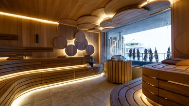 Modern gestaltete Sauna im Zauchenseehof mit runden Holzelementen, stimmungsvoller Beleuchtung und Blick nach draußen.