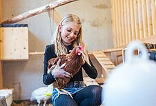 Mädchen streichelt ein Huhn im Familienhotel Almfamilyhotel Scherer in Tirol.