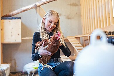 Mädchen streichelt ein Huhn im Familienhotel Almfamilyhotel Scherer in Tirol.