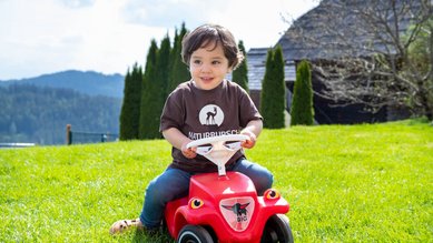 Ein kleiner Junge sitzt auf einem roten Bobbycar im Familienhotel Petschnighof in Kärnten