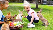 Zwei Kinder sitzen mit einem Gemüsekorb im Hasengehege und füttern die Tiere im Familienhotel Alphotel Tyrol Wellness & Family Resort in Südtirol.