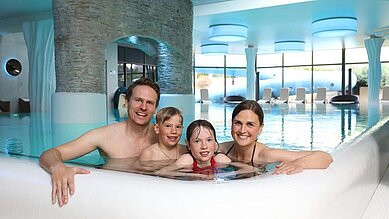 Zwei fröhliche Kinder spielen mit Wasserattraktionen in einem Kinderbeckenbereich des Hotels Feldberger Hof, spritzendes Wasser und leuchtende Farben im Hintergrund.