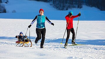 Mutter hat mit ihren beiden Kindern Spaß im Schnee im Winterurlaub in Vorarlberg.