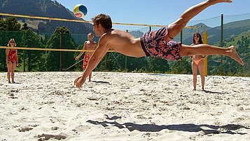 Familie spielt auf dem Volleyballplatz an einem Sommertag Volleyball und genießen den Aufenthalt im Familienhotel Sonngastein in Bad Gastein.