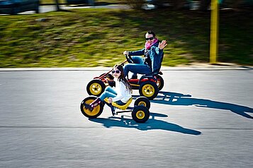 Kinder fahren mit ihren Karts ein Rennen auf dem Hof vom Familienhotel Kolping Hotel Spa & Family Resort in Ungarn.