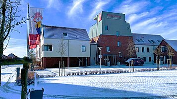 Ansicht des Familienhotels Deichkrone an der Nordsee im Winter. Das Hotel ist umgeben von verschneiter Landschaft.