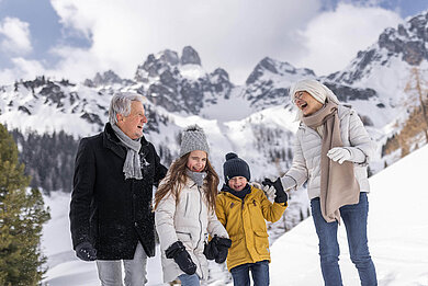 Winter im Salzburger Land: Familie macht mit Opa eine Winterwanderung in Filzmoos. Im Hintergrund ein eindrucksvolles Bergpanorama.