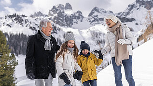 Winter im Salzburger Land: Familie macht mit Opa eine Winterwanderung in Filzmoos. Im Hintergrund ein eindrucksvolles Bergpanorama.