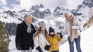 Winter im Salzburger Land: Familie macht mit Opa eine Winterwanderung in Filzmoos. Im Hintergrund ein eindrucksvolles Bergpanorama.