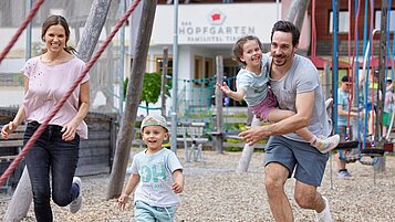 Die junge Familie tobt auf dem Spielplatz des Familienhotels Das Hopfgarten in Tirol.