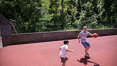 Jugendlicher Junge spielt mit seinem Vater Basketball auf dem Basketballplatz des Kinderhotels Bruckwirt.