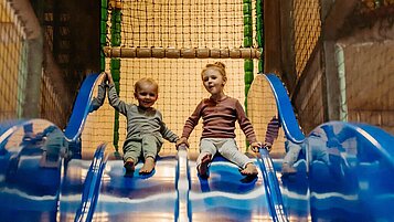 Zwei Kinder rutschen die Doppel-Indoor-Rutsche in der Spielanlage im Landhaus Averbeck in der Lüneburger Heide hinunter.