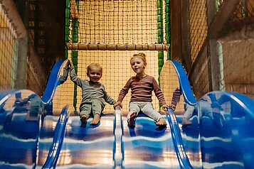 Zwei Kinder rutschen die Doppel-Indoor-Rutsche in der Spielanlage im Landhaus Averbeck in der Lüneburger Heide hinunter.