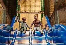 Zwei Kinder rutschen die Doppel-Indoor-Rutsche in der Spielanlage im Landhaus Averbeck in der Lüneburger Heide hinunter.