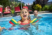 Kinder spielen mit ihrem Vater im Außenschwimmbad im Familienhotel Amiamo im Salzburger Land.