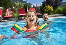 Kinder spielen mit ihrem Vater im Außenschwimmbad im Familienhotel Amiamo im Salzburger Land.