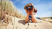 Junge liegt mit einem Fernglas in den Dünen mit Blick auf die Nordsee