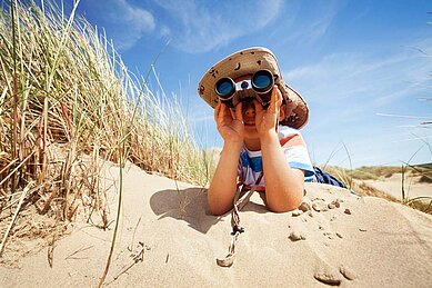 Junge liegt mit einem Fernglas in den Dünen mit Blick auf die Nordsee