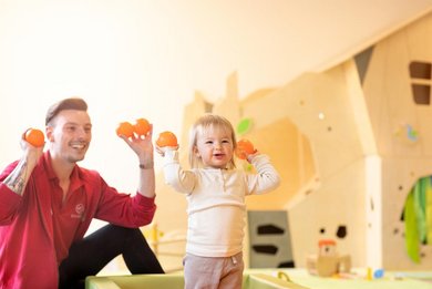 Kinderbetreuer und Kleinkind spielen gemeinsam mit Bällen im Happy-Club des Familienhotels Sonnenpark.