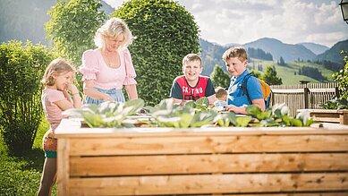 Kinder stehen gemeinsam mit einer Kinderbetreuerin im Gemüsegarten des Familienhotels Landgut Furtherwirt