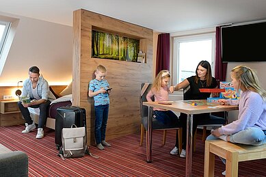 Großes Familienzimmer im Familienhotel Rhön Feeling mit drei Einzelbetten und einem Doppelbett. Der Vater steht im Raum und auf einem Einzelbett liegt seine Tochter und liest ein Buch.