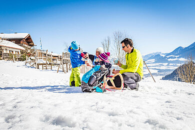 Eltern sitzen mit ihren beiden Kindern auf einem Schlitten im Schnee.