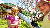 Zwei Mädchen sind im Gesicht bemalt und stehen vor einer Rutsche auf dem Spielplatz des Familienhotel Spa- & Familien-Resorts Krone im Allgäu ausklingen.