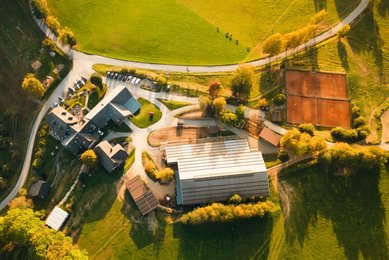 Luftaufnahme vom Familienhotel Ponyhof in Kärnten mit Reithalle, Tennisplätzen und umliegender Herbstlandschaft.