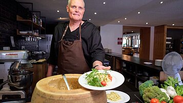 Restaurant Mitarbeiter im Familienhotel Schreinerhof bereitet frische Pasta aus dem Parmesanleib vor.