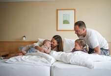 Familie mit zwei kleinen Kindern kuschelt gemeinsam im Zimmer des Familienhotel Sonne Bezau.