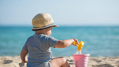 Baby spielt mit Sand am Strand an der Ostsee.