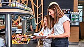 Mutter und Tochter bedienen sich am Buffet im Restaurant des Familienhotels Aigo welcome family in Oberösterreich