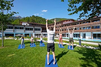 Zusammen mit einem Trainer machen Erwachsene und Kinder Bewegungsübungen im Garten des Familienhotel Das Bayrischzell in Oberbayern