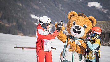 Vater und Tochter beim Skifahren in den Dolomiten gemeinsam mit dem Maskottchen des Familienhotels Alpenhof Dolomit Family