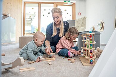 Mutter spielt im Babyzimmer mit ihrem Baby und Kleinkind mit den altersgerechten Spielsachen im Familienhotel Almfamilyhotel Scherer in Tirol.