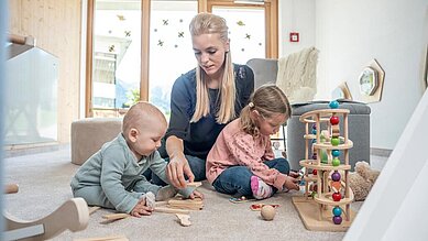 Mutter spielt im Babyzimmer mit ihrem Baby und Kleinkind mit den altersgerechten Spielsachen im Familienhotel Almfamilyhotel Scherer in Tirol.