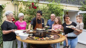 Mehrere Leute stehen vor einem großen Grill, auf dem leckeres Fleisch und Gemüse gegrillt wird.