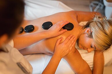 Eine Frau bekommt eine Hot Stone Behandlung im Wellnessbereich im Familienhotel Das Bayrischzell in Oberbayern